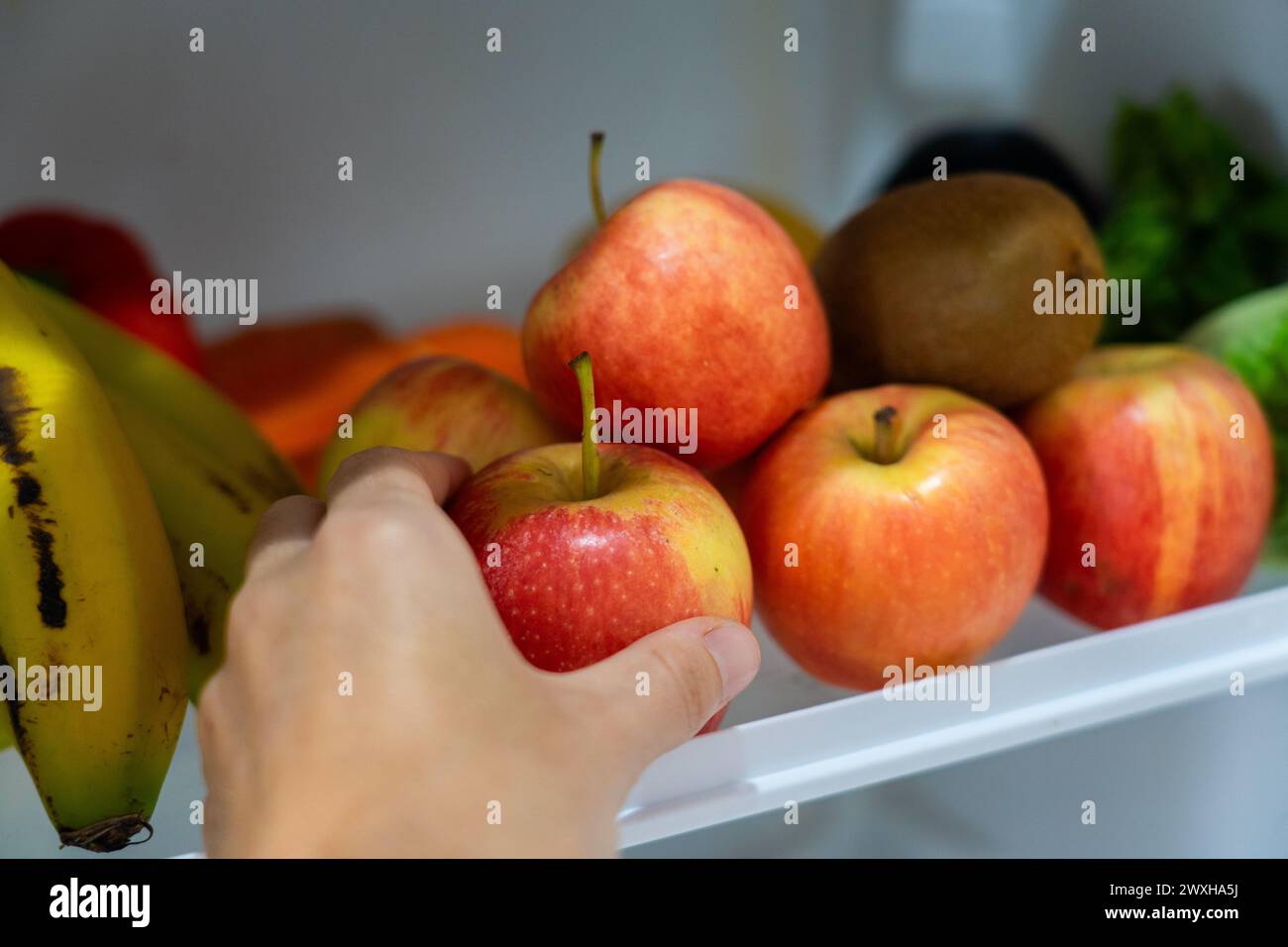 Hand einen Apfel aus einem Kühlschrankregal mit gesundem veganem Essen holen Stockfoto