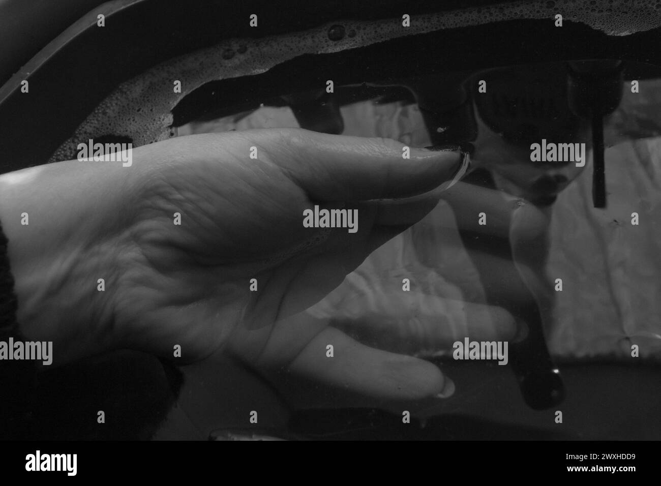 Schwarz-weiß-Nahaufnahme einer Handpalme nach oben, die in Wasser mit Reflexionen und Copyspace getaucht ist. Stockfoto