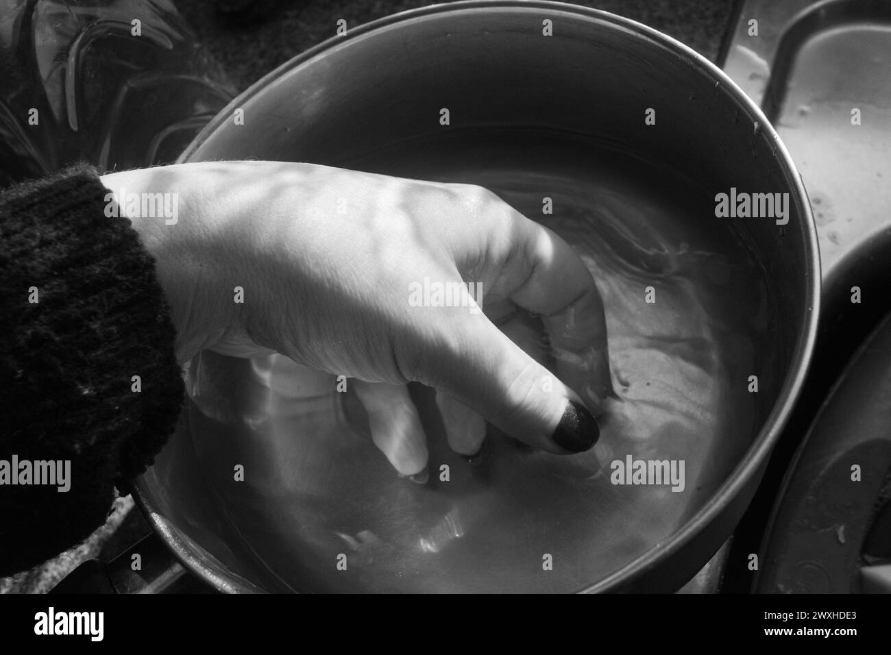Waschen einer Hand - Schwarz-weiß-Aufnahme einer Hand im Inneren eines Metallkassers, der in Wasser mit kontrastierendem Licht und Schatten getaucht ist. Stockfoto