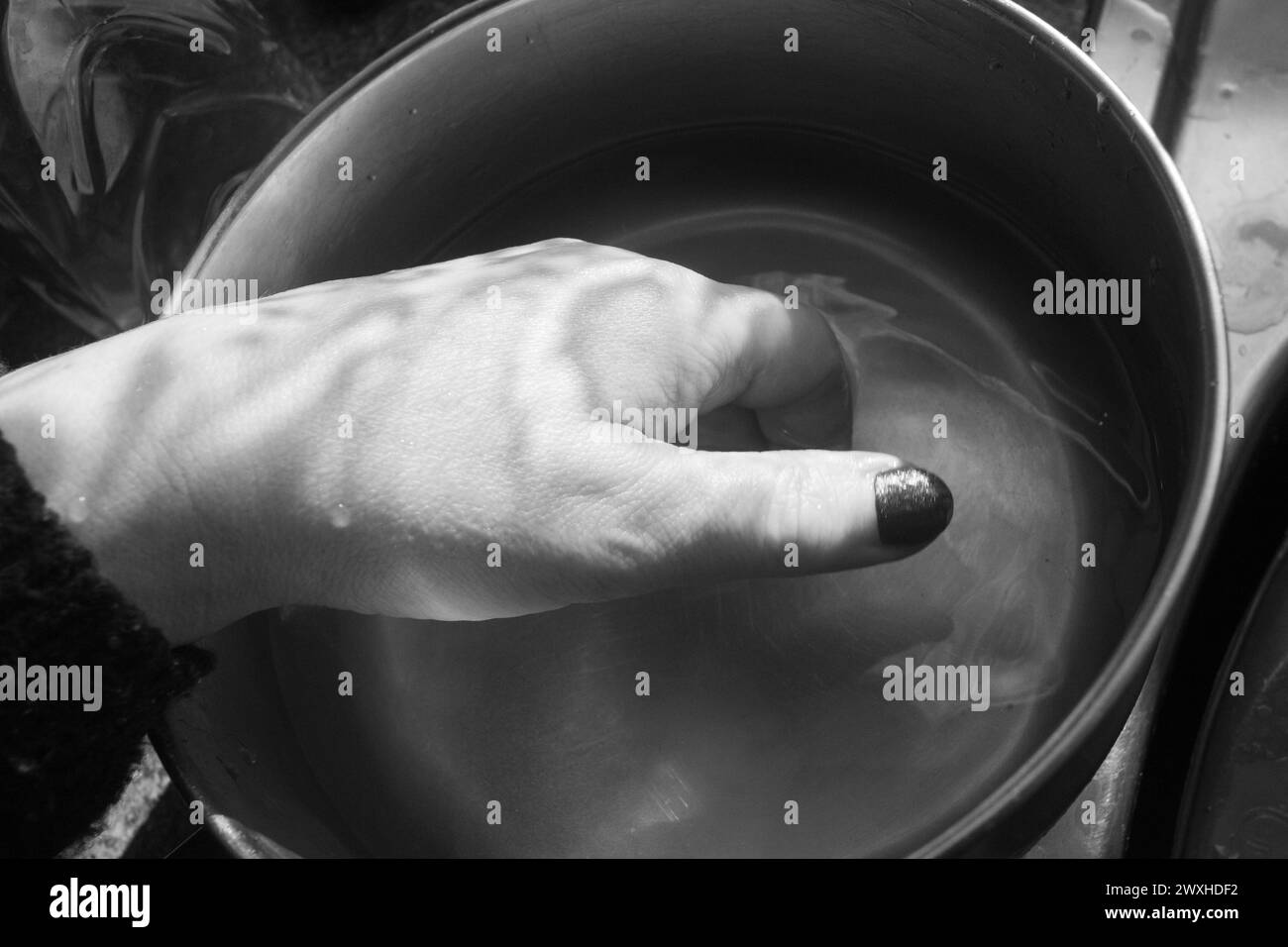 Waschen einer Hand - Schwarz-weiß-Aufnahme einer Hand im Inneren eines Metallkassers, der in Wasser mit kontrastierendem Licht und Schatten getaucht ist. Stockfoto