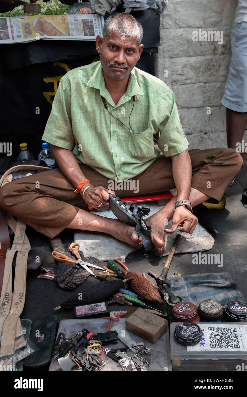 Indischer Mann repariert Schuhe auf der Straße, auch Schuhmacher, Schuster oder Mochi genannt. Schuhmacher arbeitet an einem Paar Schuhen in den Straßen von Mumbai India-Ma Stockfoto