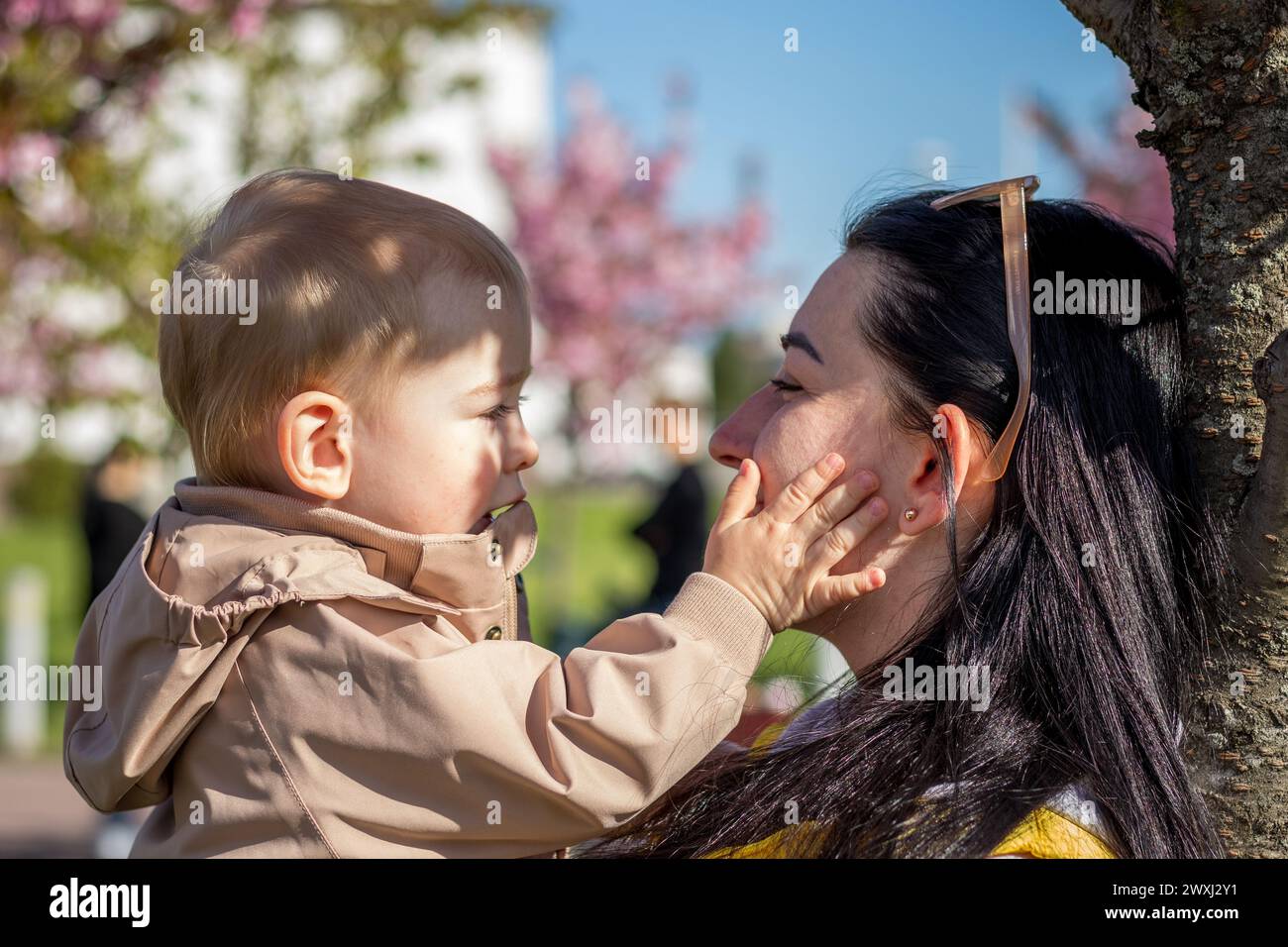 Eine glückliche Mutter und ein Kind laufen unter den Zweigen eines Kirschbaums Stockfoto