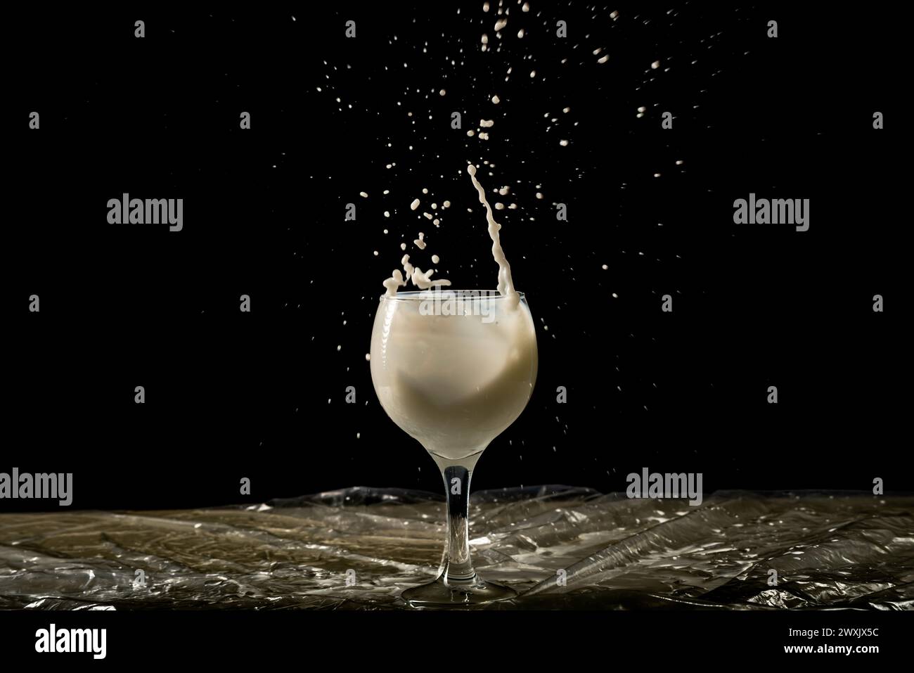 Spritzen Sie in einen Glasbecher mit Milch hinein. Stürze fliegen in verschiedene Richtungen. Isoliert auf schwarzem Hintergrund. Stockfoto