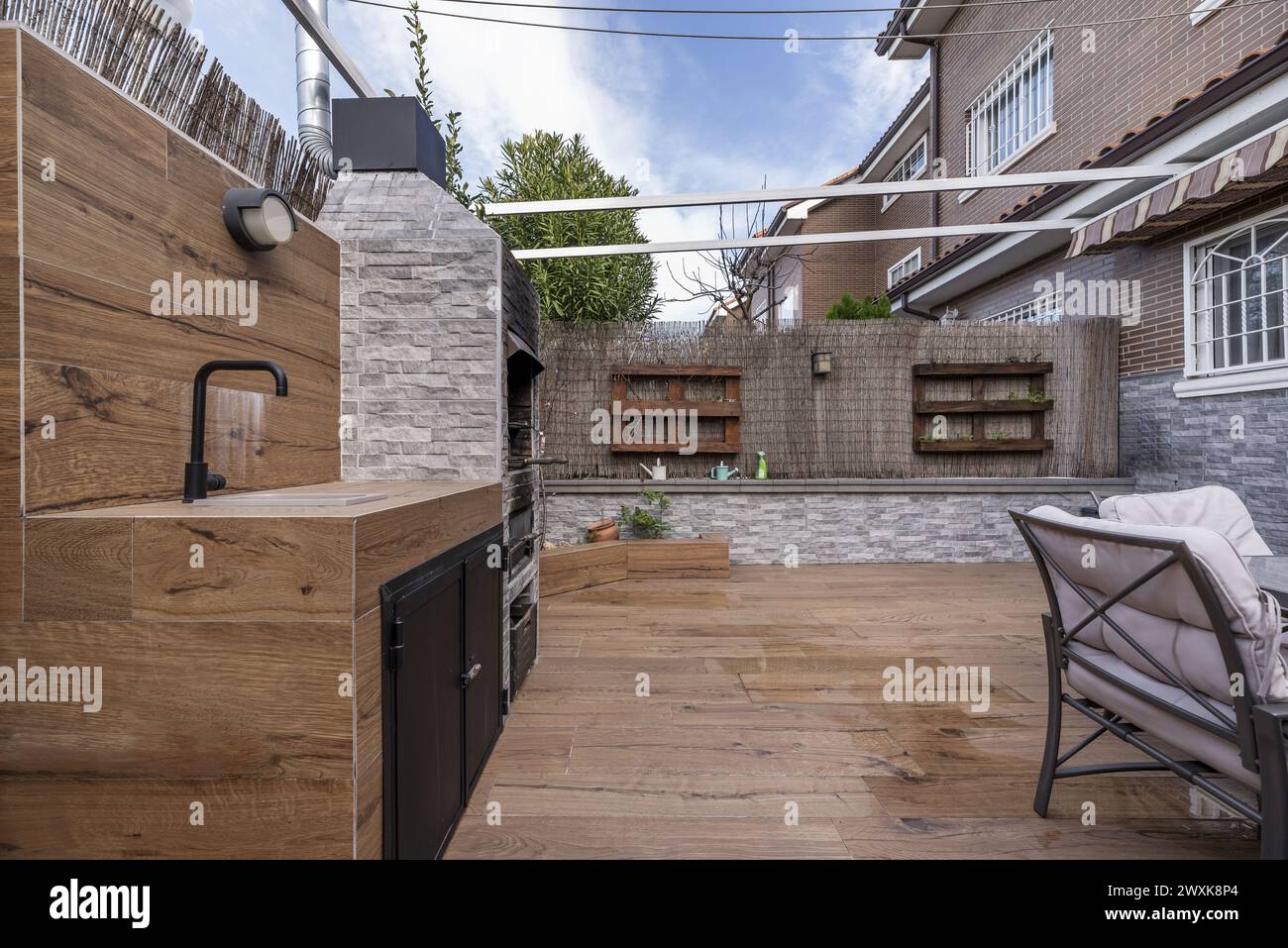 Hinterhof eines Einfamilienhauses mit Fußböden aus imitiertem Holzsteinzeug, Esstisch im Freien und eingebautem Grill Stockfoto