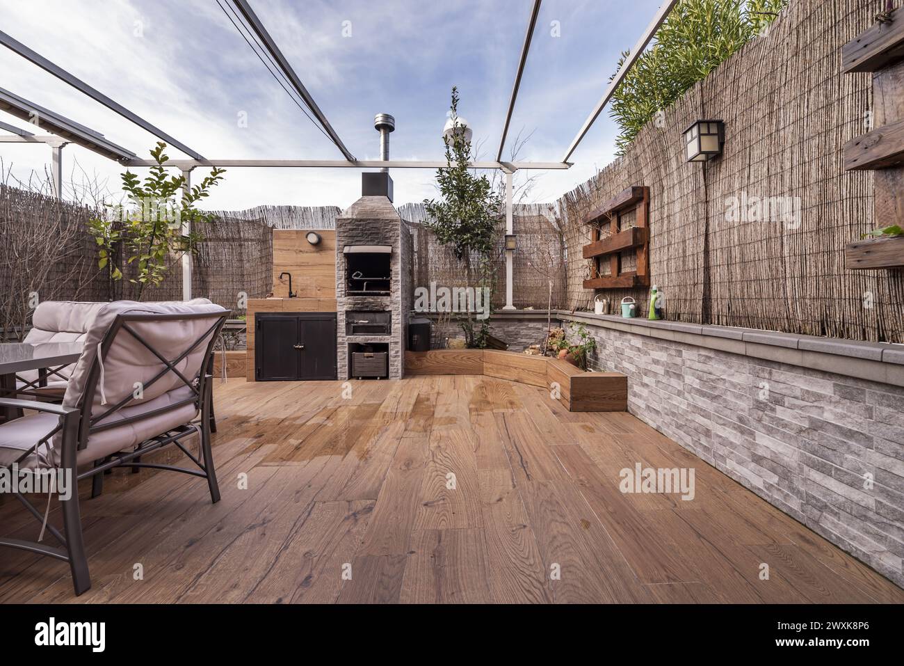 Ein Hinterhof eines Einfamilienhauses mit Fußböden aus imitiertem Holzsteinzeug und dekorativen Holzmöbeln, einem grauen Stoffsofa und einem eingebauten Grill Stockfoto