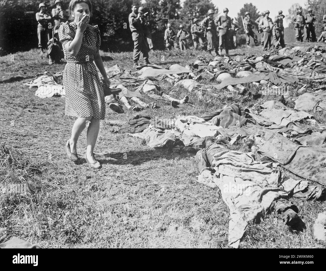 Ein deutsches Mädchen wird überfallen, als sie an den exhumierten Leichen einiger der 800 von SS-Wärtern ermordeten Sklavenarbeiter in der Nähe von Namering vorbeigeht und hier liegt, damit die Bürger die Arbeit ihrer Nazi-Führer sehen können. Mai 1945 Stockfoto
