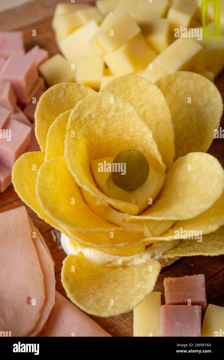 Schinken- und Kartoffelchips auf einem Holzbrett mit einer dekorativen gelben Rose aus Chips angeordnet Stockfoto