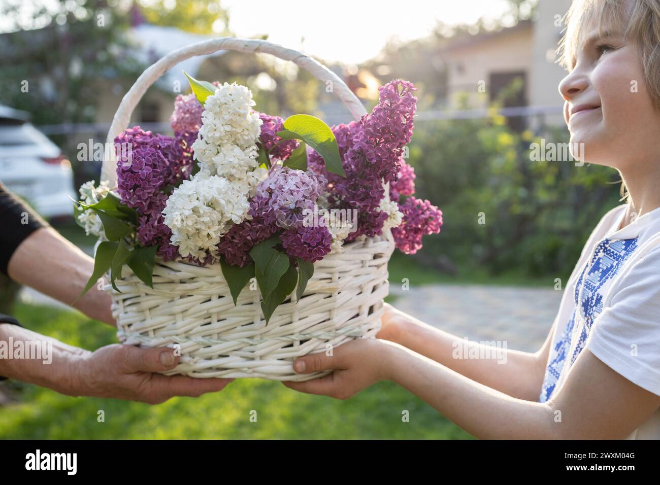 Der Junge hält einen Korb mit blühenden Zweigen aus weißem und violettem Flieder als Geschenk für seine Mutter oder Großmutter aus. Positive Atmosphäre, Freude, fes Stockfoto