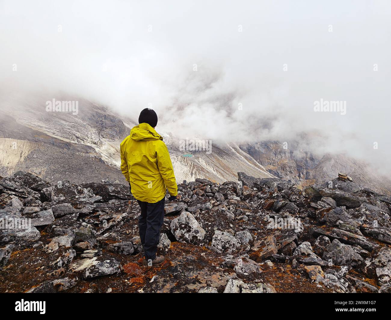 Person in gelber Jacke mit Blick auf die nebelige Himalaya-Landschaft. Stockfoto