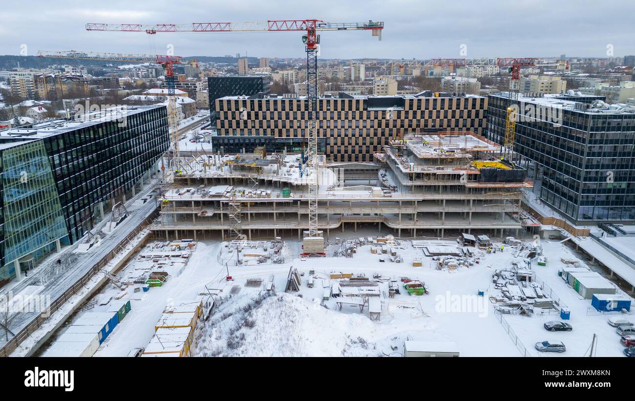 Drohnenfotografie von Baustellen umgeben von Gebäuden in einer Stadt, die während des bewölkten Wintertages von Schnee bedeckt ist Stockfoto