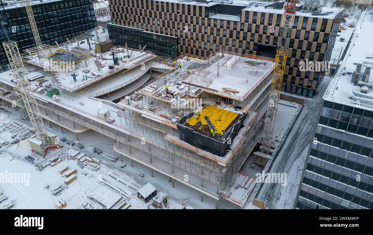 Drohnenfotografie von Baustellen umgeben von Gebäuden in einer Stadt, die während des bewölkten Wintertages von Schnee bedeckt ist Stockfoto