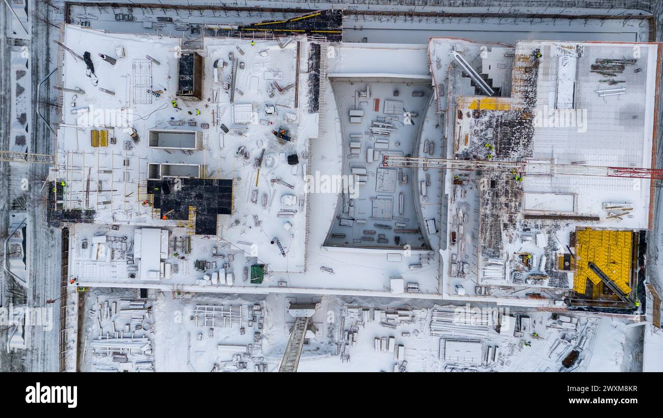 Drohnenfotografie von Baustellen umgeben von Gebäuden in einer Stadt, die während des bewölkten Wintertages von Schnee bedeckt ist Stockfoto