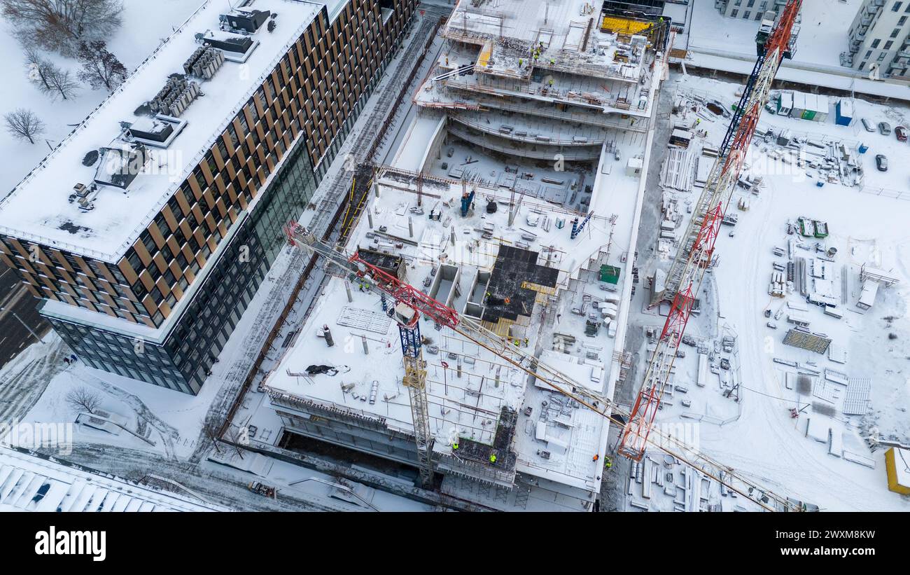 Drohnenfotografie von Baustellen umgeben von Gebäuden in einer Stadt, die während des bewölkten Wintertages von Schnee bedeckt ist Stockfoto