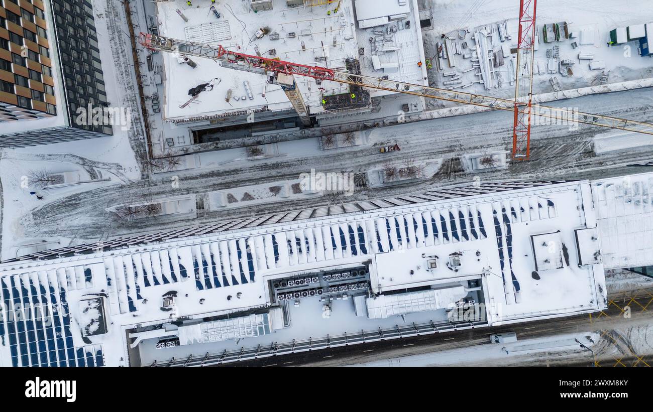 Drohnenfotografie von Baustellen umgeben von Gebäuden in einer Stadt, die während des bewölkten Wintertages von Schnee bedeckt ist Stockfoto