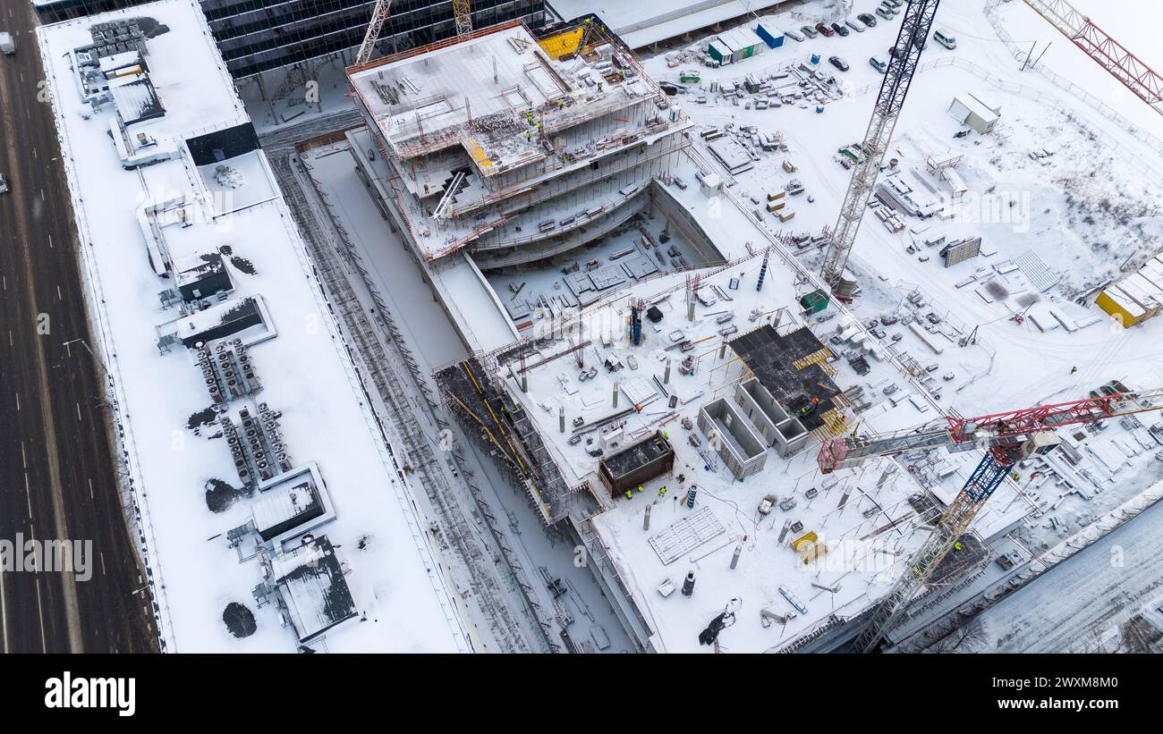Drohnenfotografie von Baustellen umgeben von Gebäuden in einer Stadt, die während des bewölkten Wintertages von Schnee bedeckt ist Stockfoto