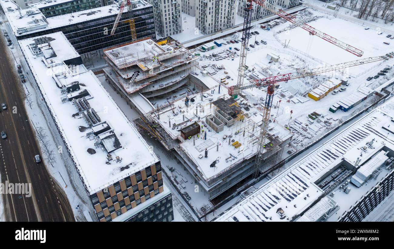 Drohnenfotografie von Baustellen umgeben von Gebäuden in einer Stadt, die während des bewölkten Wintertages von Schnee bedeckt ist Stockfoto