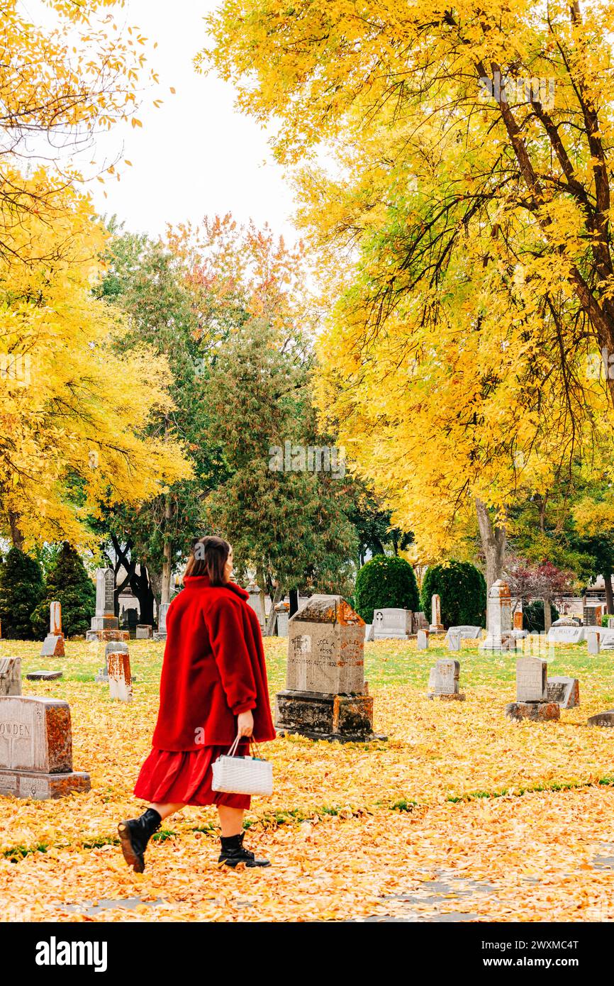 Frau in Rot, die am Herbsttag durch den Friedhof geht Stockfoto