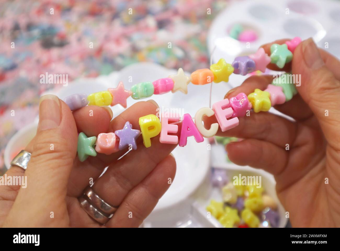 Das gerade fertig gefertigte Armband mit mehrfarbigen Perlen und dem Text PEACE in den Händen Stockfoto
