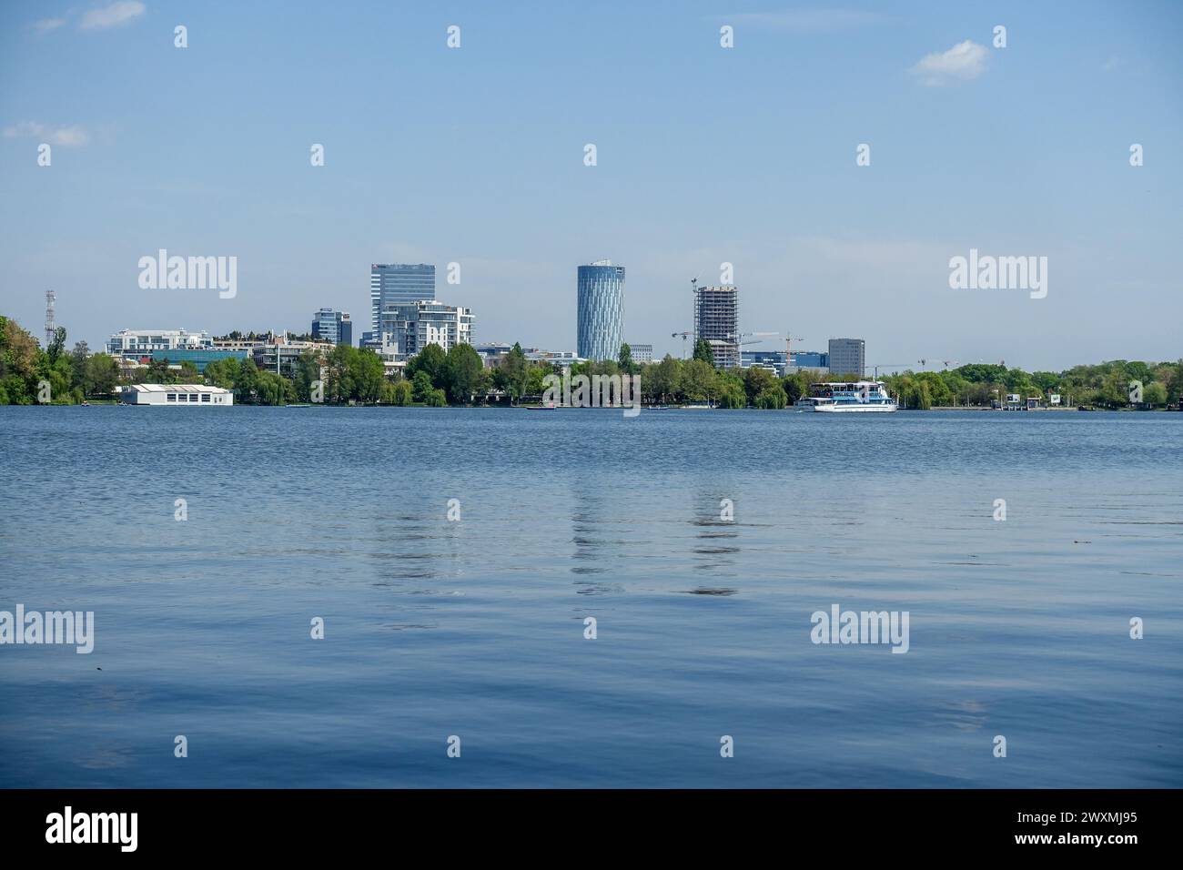 Blick auf die Skyline von Bukarest von einem ruhigen Herastrau-See mit modernen Hochhäusern und üppigem Grün im Hintergrund in Rumänien Stockfoto