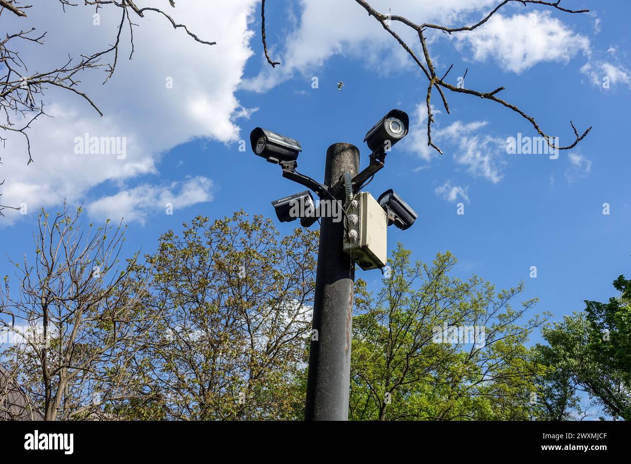 Überwachungskameras, die an einem Pfosten montiert sind, überwachen einen öffentlichen Park in Bukarest, Rumänien, an einem sonnigen Tag mit blauem Himmel und verstreuten Wolken Stockfoto