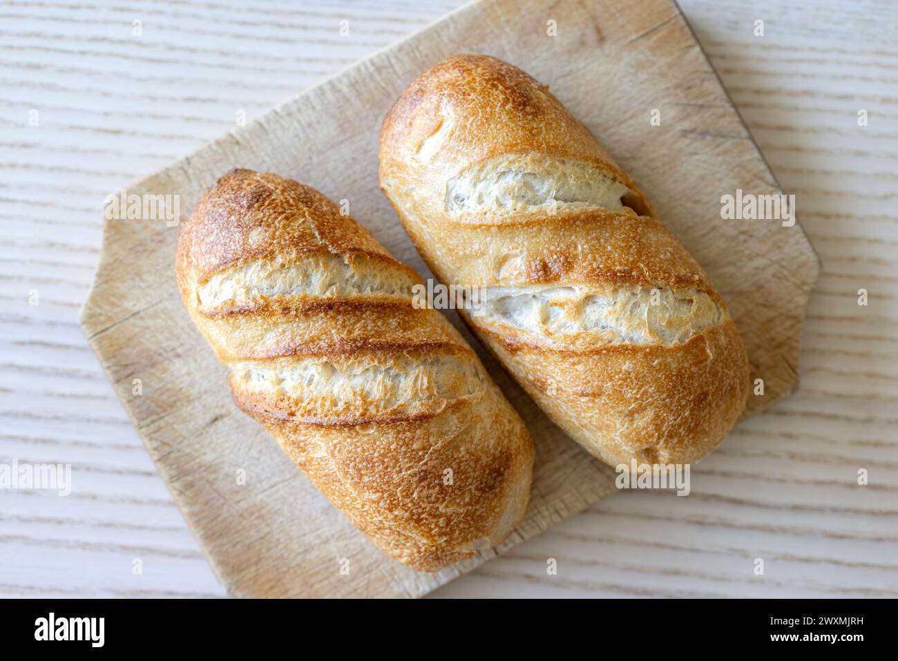 Zwei knusprige goldbraune Brotlaibe auf hölzernem Schneidebrett - Blick von oben. Stockfoto