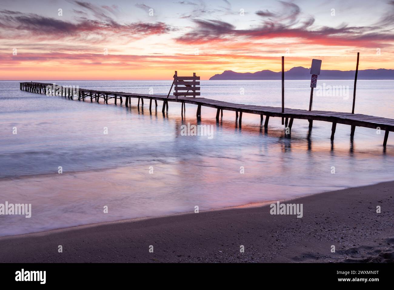 Wunderschöner Sonnenaufgang an einem Strand mit altem Holzsteg in Platja de Muro, Mallorca, Balearen, Spanien Stockfoto