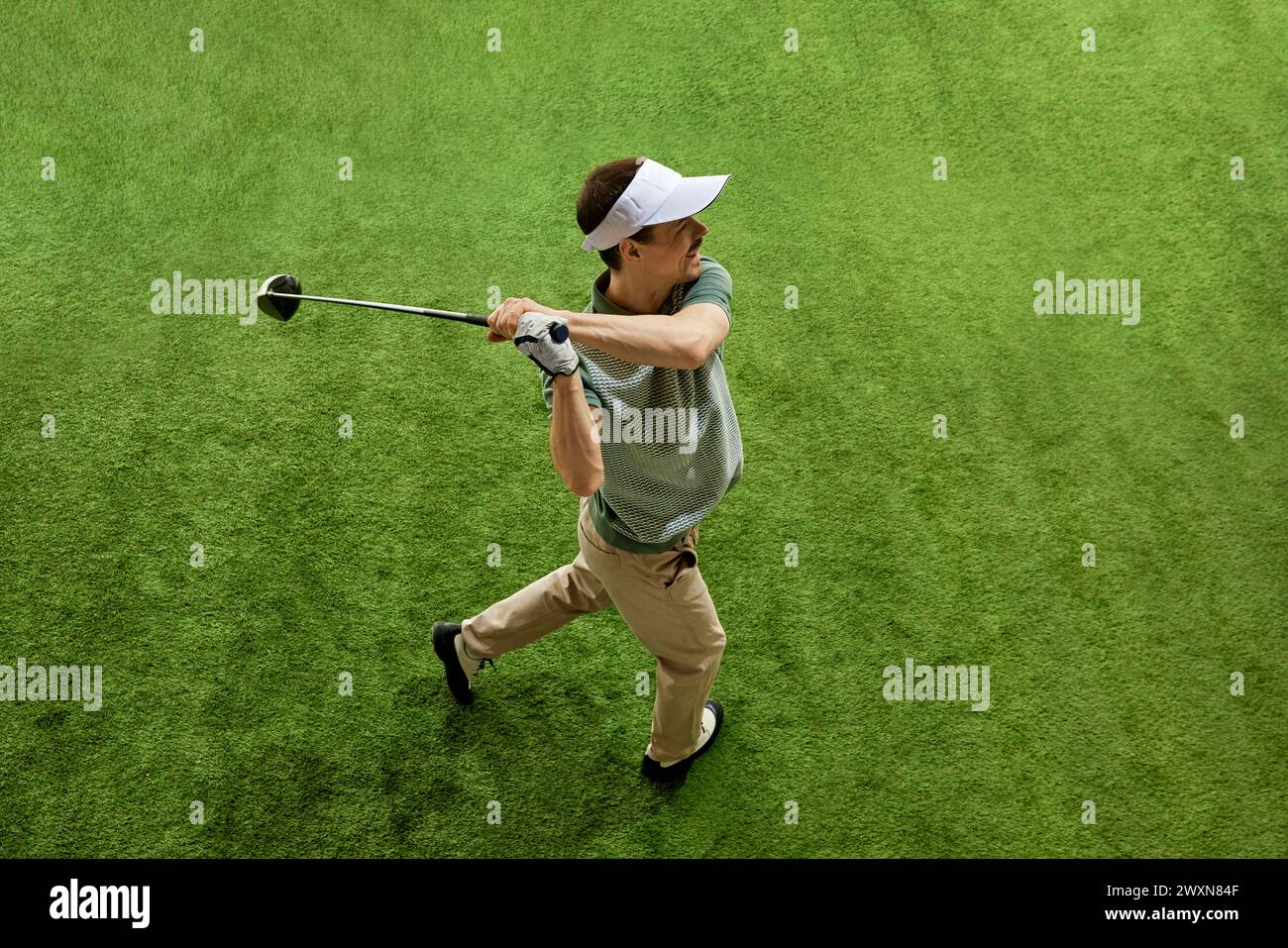 Geschickt, fokussiert auf den Golfspieler von oben am Ende des Schwungs posiert auf dem üppig grünen Golfplatz. Männliches Modell mit Blick auf die Entfernung. Stockfoto
