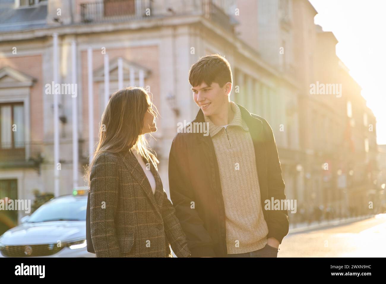 Junge Paare, die Hand in Hand durch die Stadt laufen, mit der Sonne im Hintergrund Stockfoto