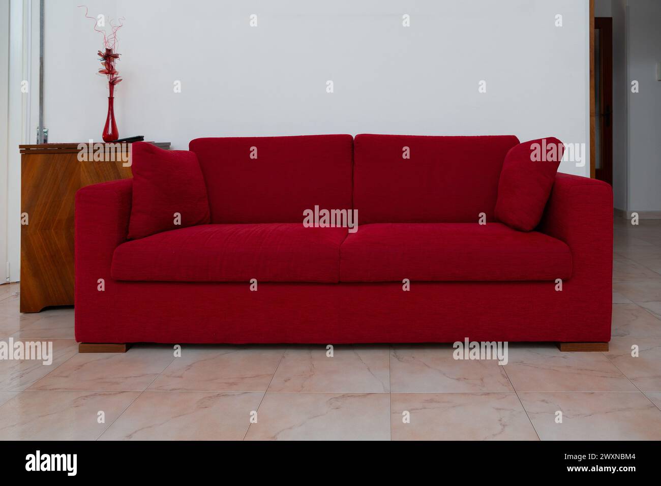 Ein stilvolles rotes Sofa bietet Farbakzente und ein minimalistisches Dekor, das zeitgenössisches Wohndesign widerspiegelt Stockfoto