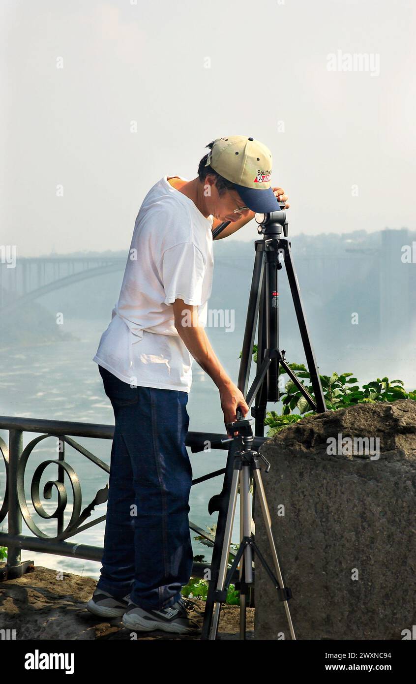 Das Stockfoto zeigt einen asiatischen Fotografen, der sein Stativ an den Niagarafällen in Kanada aufstellt. Stockfoto