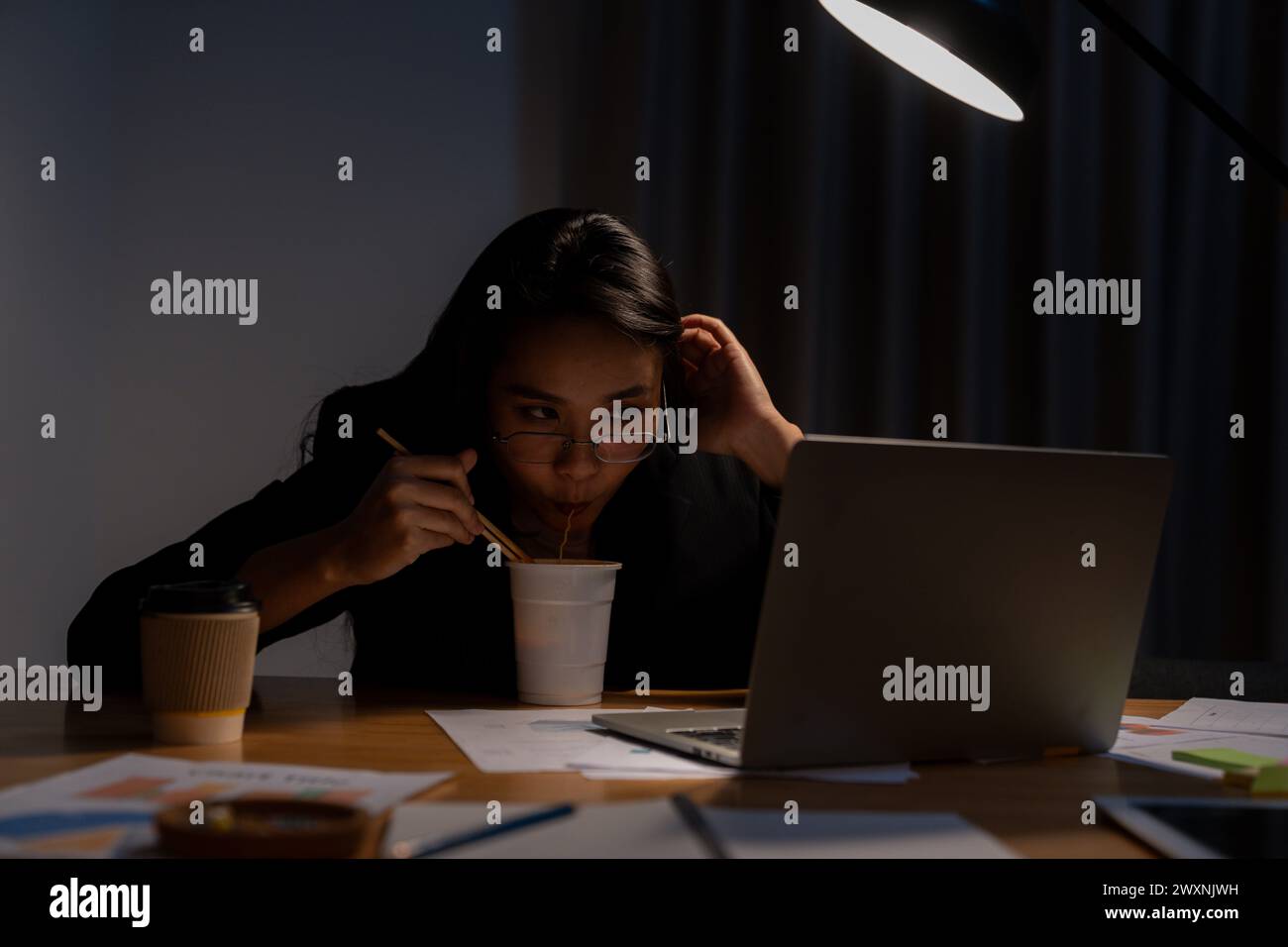 Die junge Frau arbeitete spät und isst jetzt Instant-Nudeln im Büro Stockfoto