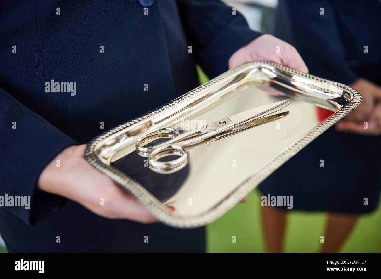 Hände halten ein silbernes Tablett mit der Schere Stockfoto