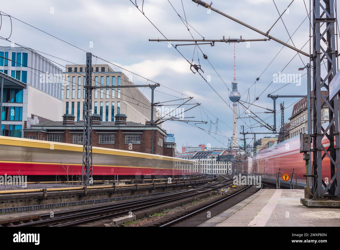 An einem kühlen Frühlingstag fahren die Züge in Unschärfe ab und nähern sich dem Bahnhof Berlin Friedrichstraße. Typische Häuser und Fernsehturm im bac zu sehen Stockfoto