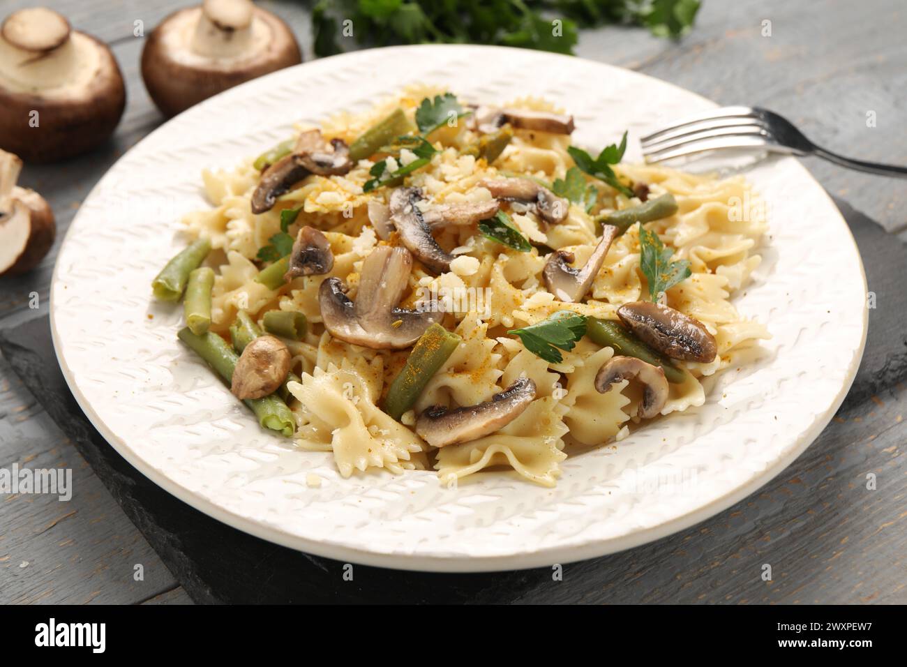 Vegetarische Pasta mit Pilzen, Petersilie, Bohnen und Käse auf grauem Holztisch, Nahaufnahme Stockfoto