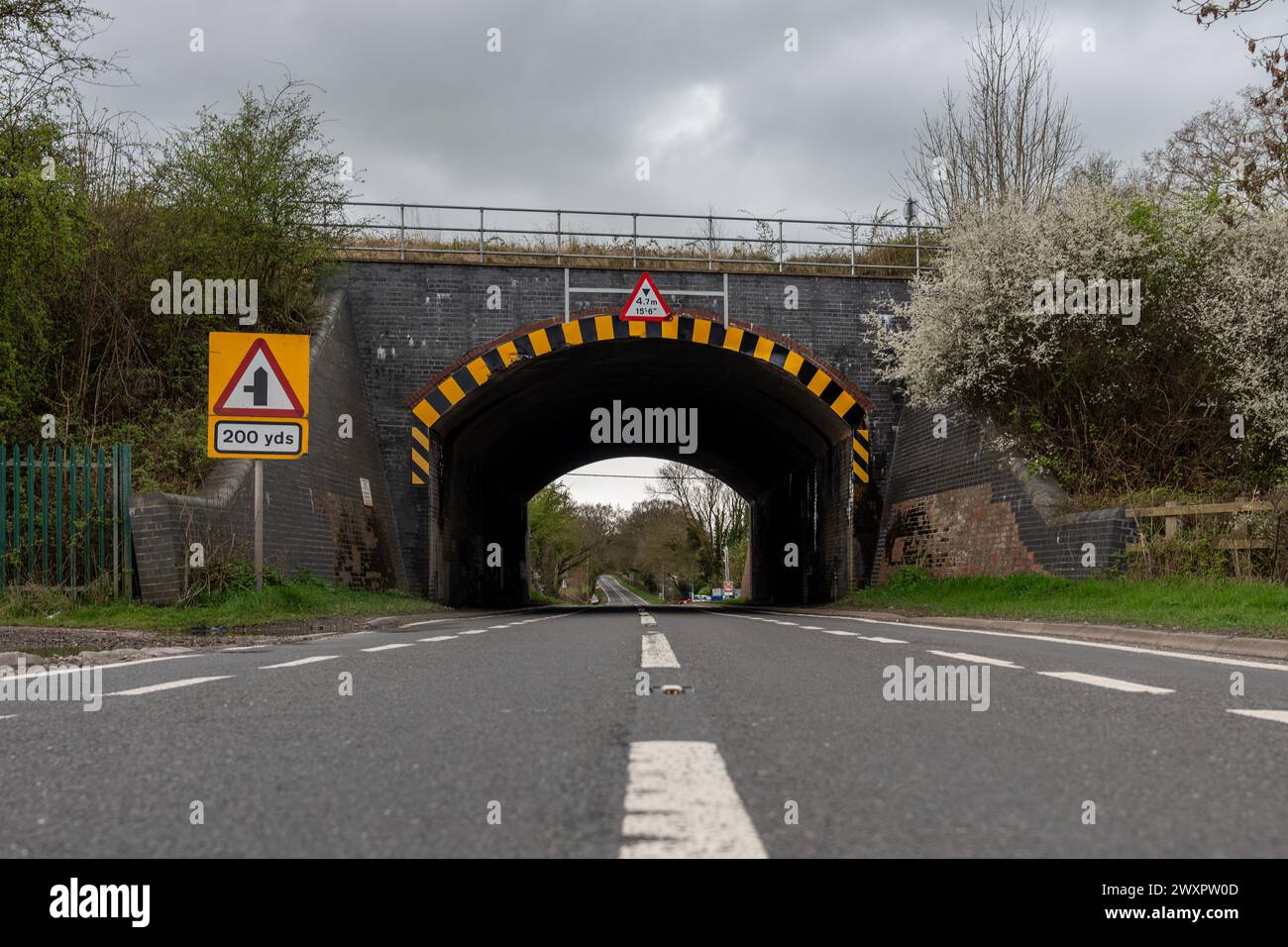 Blick auf die Straße mit einem Warnschild für eine niedrige Brücke 200 m vor einem ländlichen Hintergrund mit blühenden Bäumen Stockfoto