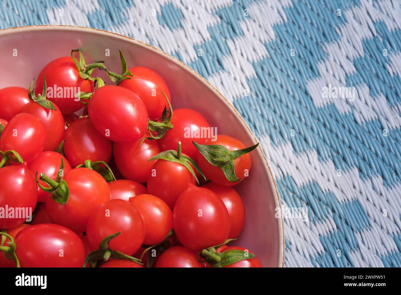 Eine Schüssel mit frischen Bio-Tomaten auf gewebtem Hintergrund mit geometrischen Mustern in Grün und weiß. Stockfoto