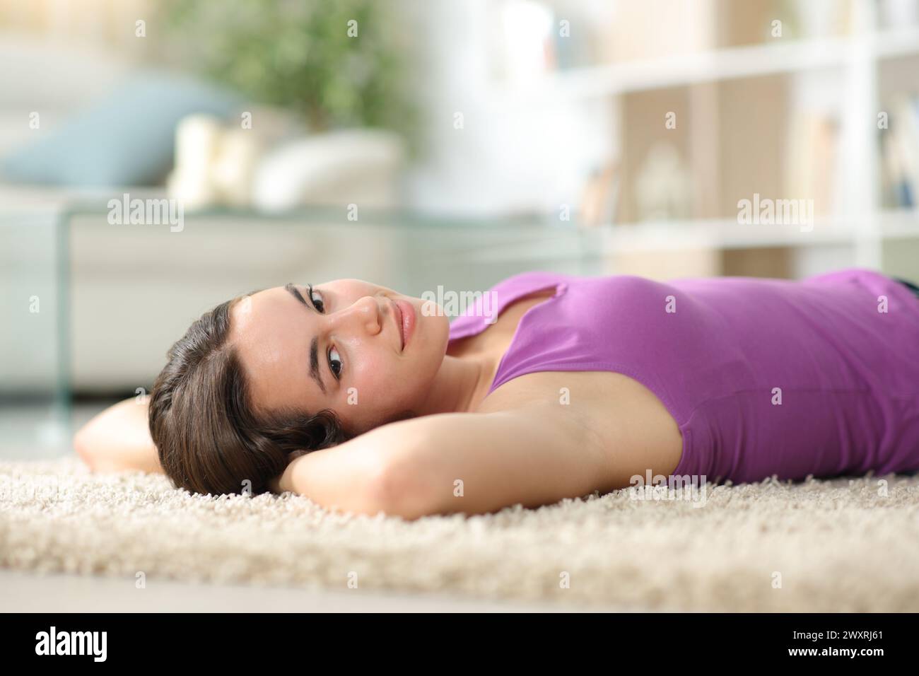 Eine zufriedene Frau sieht dich zu Hause entspannt auf einem Teppich liegen an Stockfoto