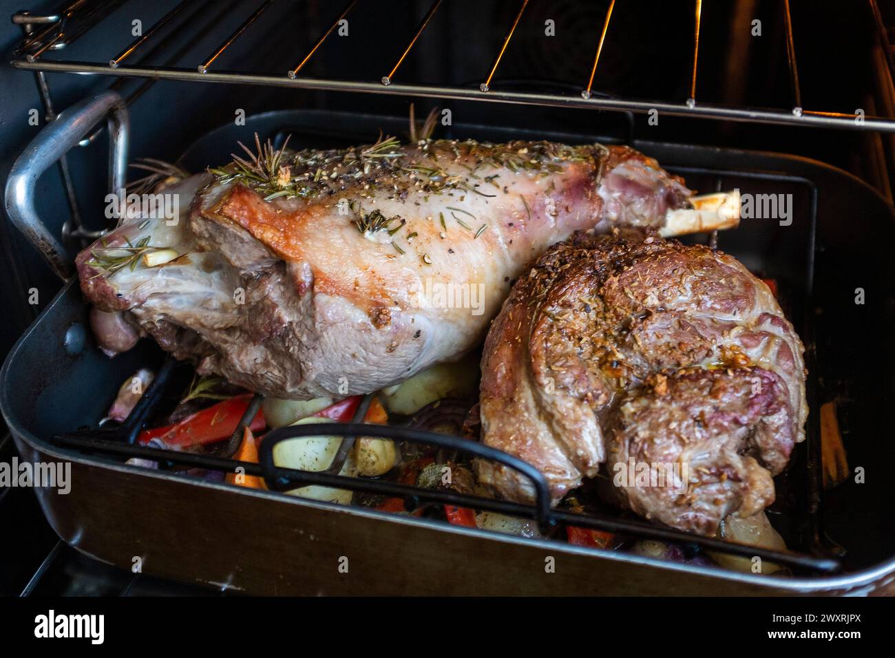 Kochen Sie ein Bein und eine kleine Lammschulter mit Knoblauch und Rosmarinkräutern in einem elektrischen Ofen mit Ventilator Stockfoto