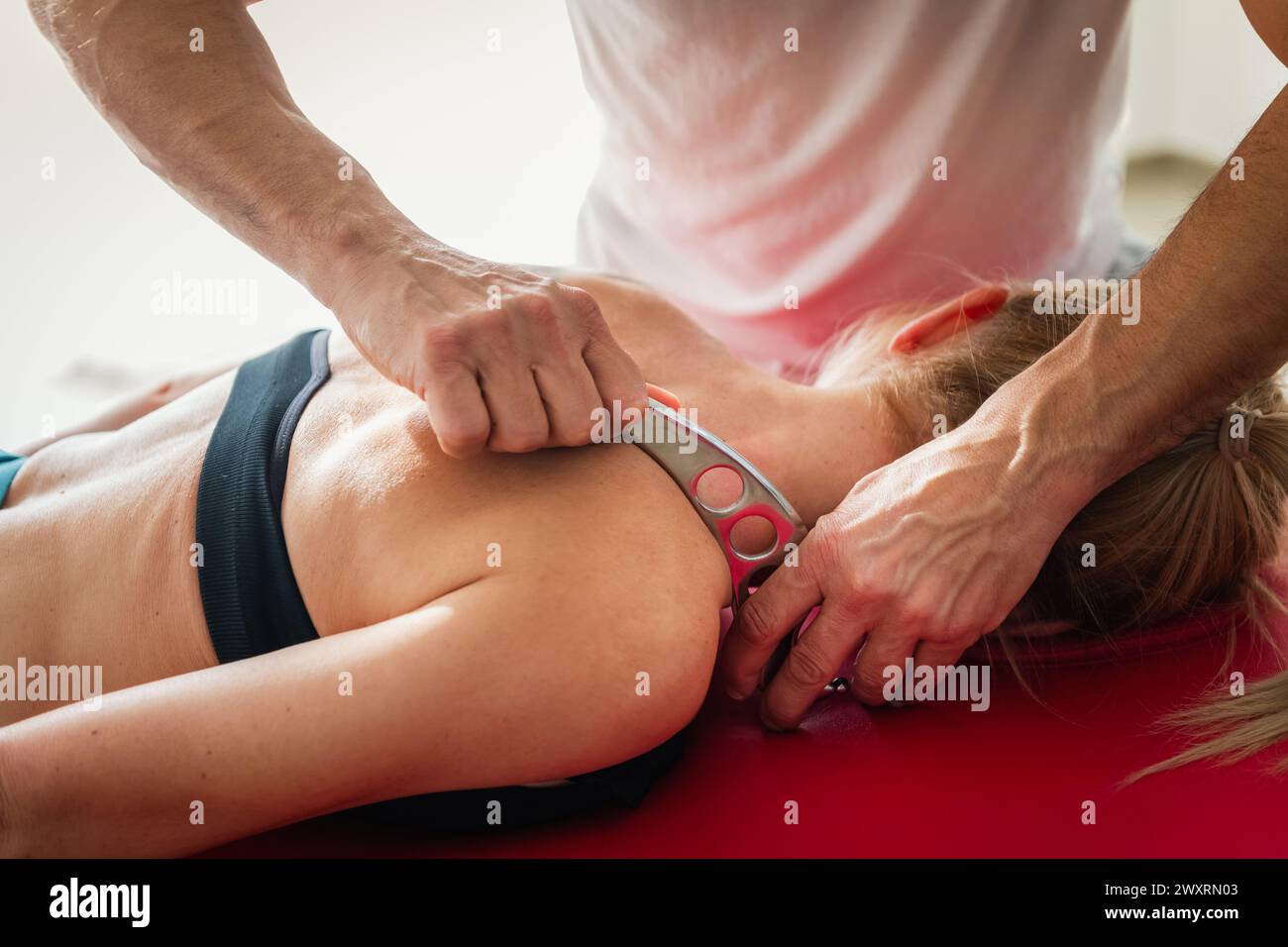 Massagetherapeutin mit IASTM-Werkzeug auf der Schulter einer im Wellnesszentrum liegenden Patientin während der Rehabilitationsbehandlung in der Therapie Stockfoto