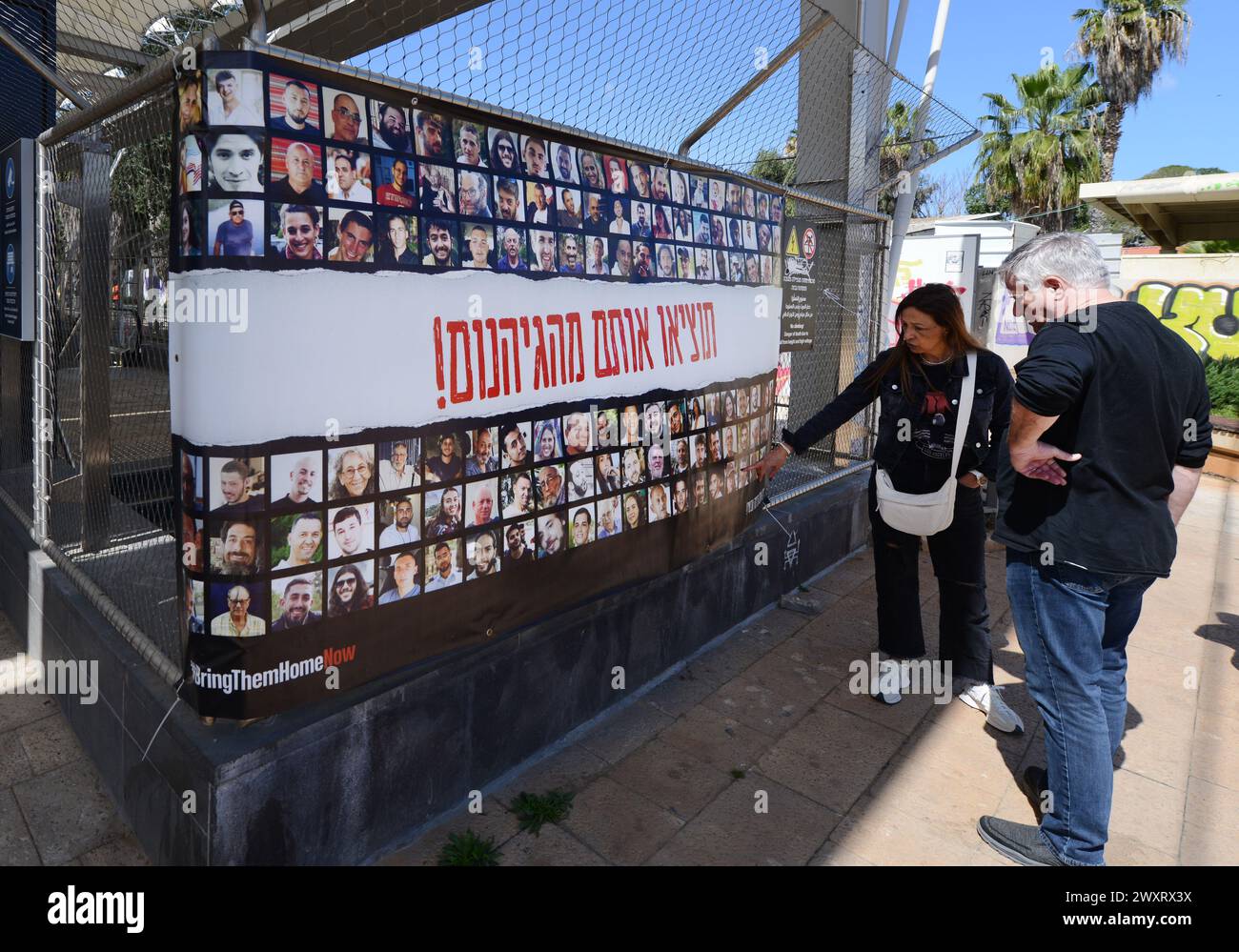 Ein Paar, das sich ein Poster mit den Bildern der israelischen Geiseln in Gaza ansieht. Park Hamesila, Tel-Aviv, Israel. Stockfoto