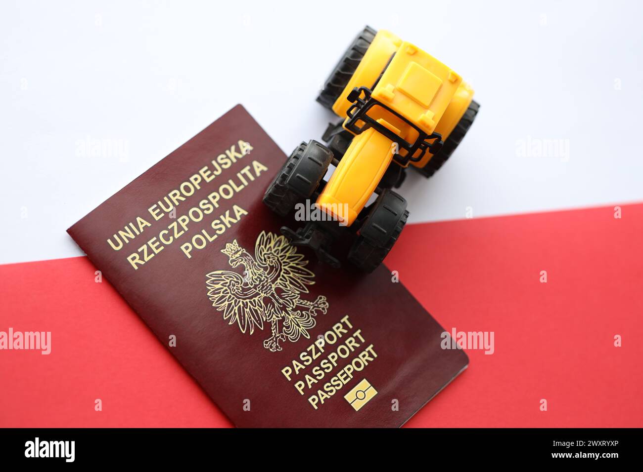 Roter polnischer Pass und gelber Traktor auf glatter rot-weißer Flagge von Polen Nahaufnahme Stockfoto