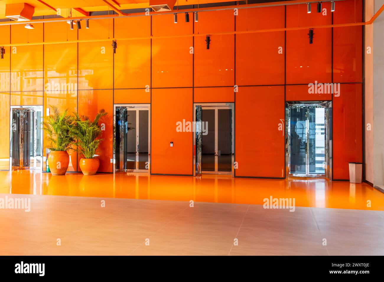 Aufzüge in orangefarbenem, glänzenden Hallenboden mit Pflanzen im Innenbereich. Stockfoto
