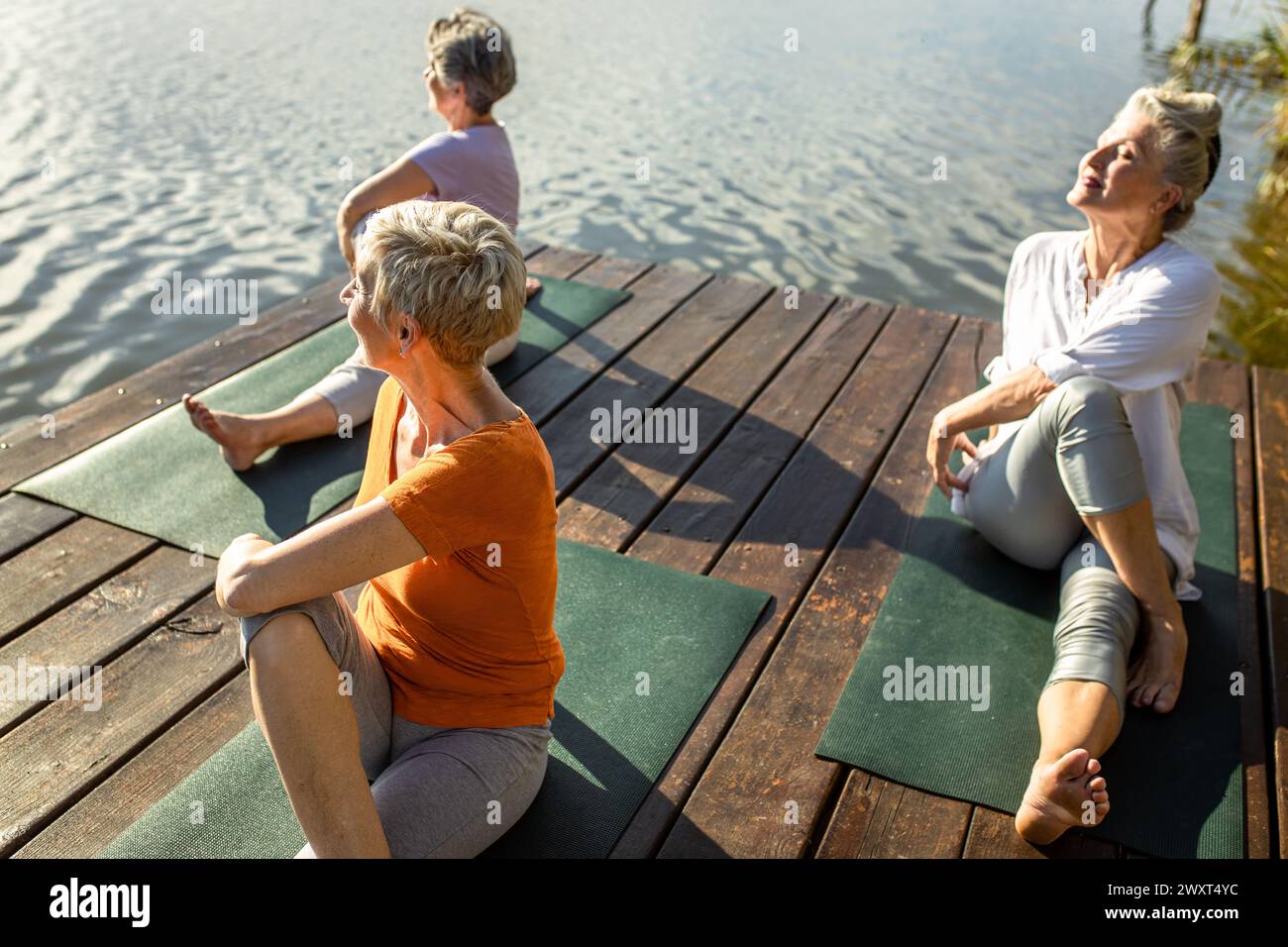 Gruppe von Seniorinnen, die Yoga-Übungen am See machen. Stockfoto