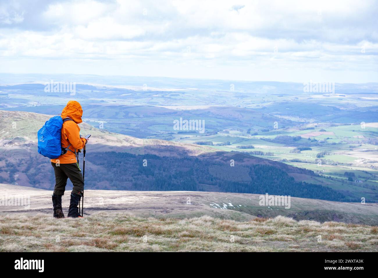 Brecon Beacons Wales. Ein einsamer Walker in bunten Wanderbekleidung, der auf dem Gipfel des Corn du steht und sein Handy überprüft, bevor er weitergeht Stockfoto