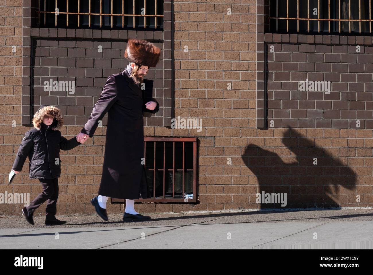 Auf Purim werfen ein chassidischer Mann und sein Sohn einen riesigen Schatten auf dem Weg zu den Morgengottesdiensten. An der Wythe Avenue in Williamsburg, Brooklyn, New York. Stockfoto