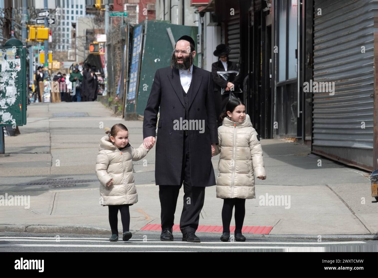 Ein chassidischer jüdischer Vater und seine gleichgekleideten Töchter überqueren eine Straße in Brooklyn, New York. Stockfoto