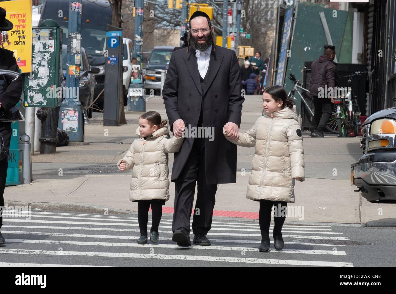 Ein chassidischer jüdischer Vater und seine gleichgekleideten Töchter überqueren eine Straße in Brooklyn, New York. Stockfoto