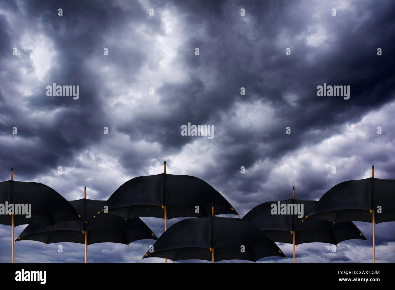 Offene schwarze Regenschirme unter einem dramatisch bewölkten und stürmischen Himmel Stockfoto