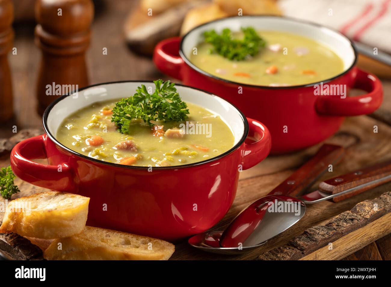 Zwei Schüsseln Erbsensuppe mit Schinken und Karotten, garniert mit Petersilie auf rustikalem Holztablett Stockfoto