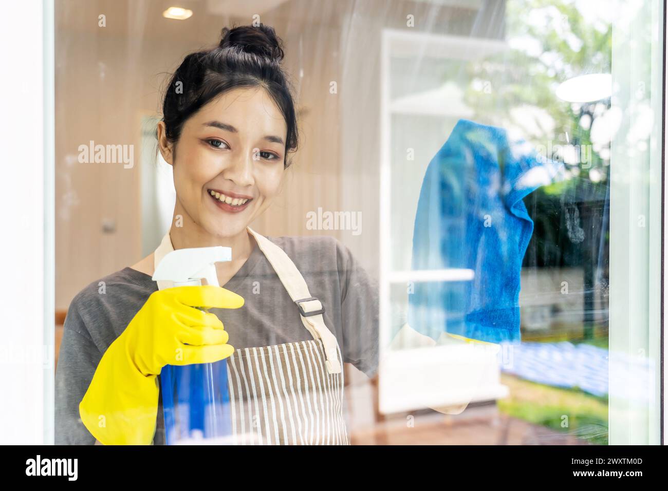 Junge Frau in Schürze und gelben Handschuhen, die Fenster reinigen Stockfoto